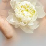 Organic Skincare - Unrecognizable female with soft manicured hands holding white flower with delicate petals in hands during spa procedures