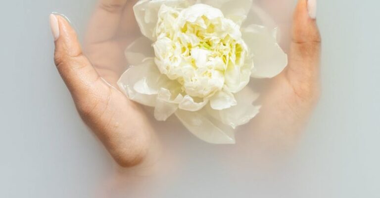 Organic Skincare - Unrecognizable female with soft manicured hands holding white flower with delicate petals in hands during spa procedures