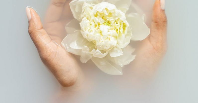 Organic Skincare - Unrecognizable female with soft manicured hands holding white flower with delicate petals in hands during spa procedures