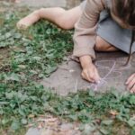 Natural Dyes - High angle of crop unrecognizable barefooted child painting on ground with colorful chalks while playing in green garden