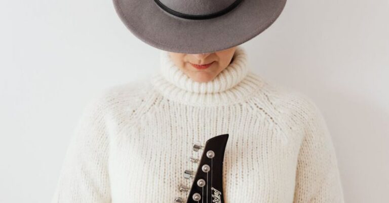 Plain Outfit - Unrecognizable female musician wearing white knitted sweater and stylish hat standing against white plain background with electric guitar fretboard in hands