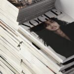 Fashion Diary - High angle many fashion magazines stacked on floor against white brick wall in studio