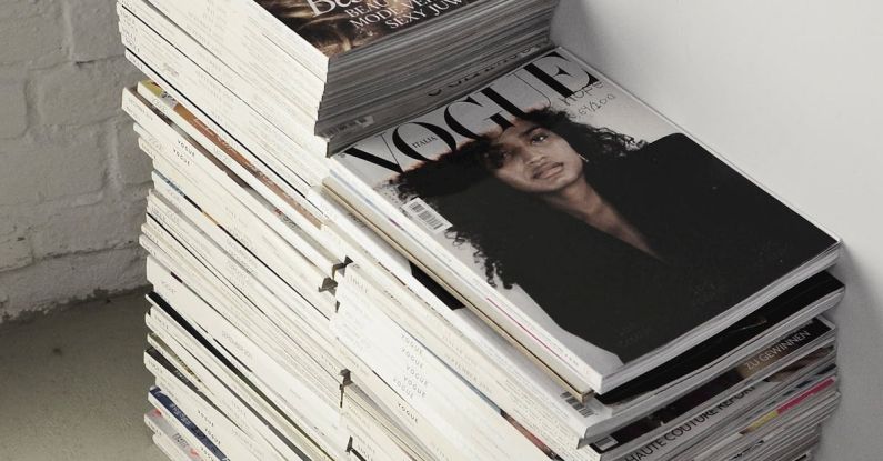Fashion Diary - High angle many fashion magazines stacked on floor against white brick wall in studio