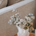 Comfort And Style - Cozy sofa with decorative cushions near stump with books and blooming flowers in vase in house room